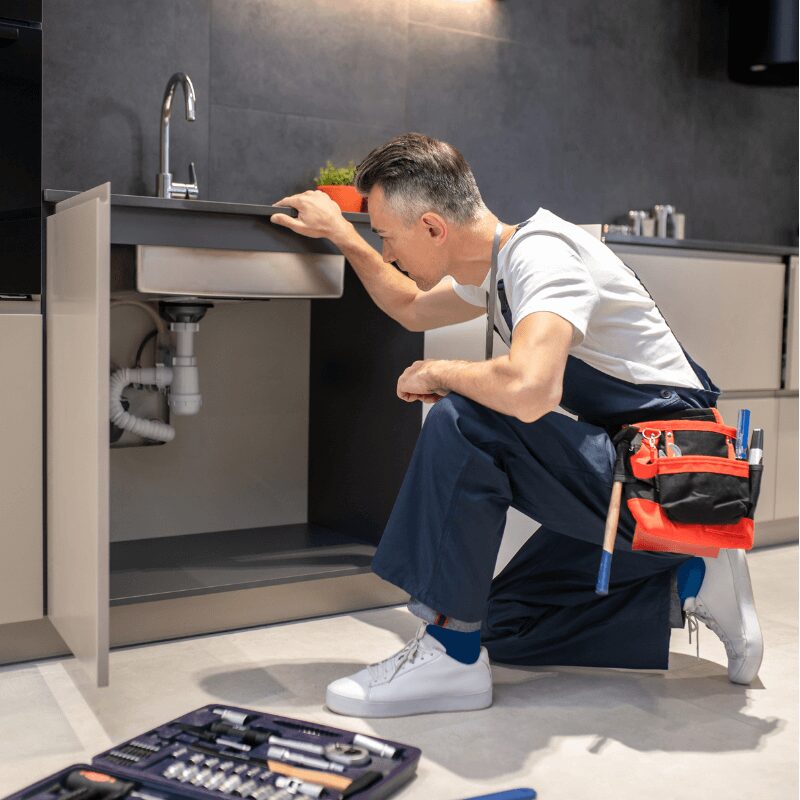 man-kneeling-down-touching-sink-inspecting-pipes man-kneeling-down-touching-sink-inspecting-pipes